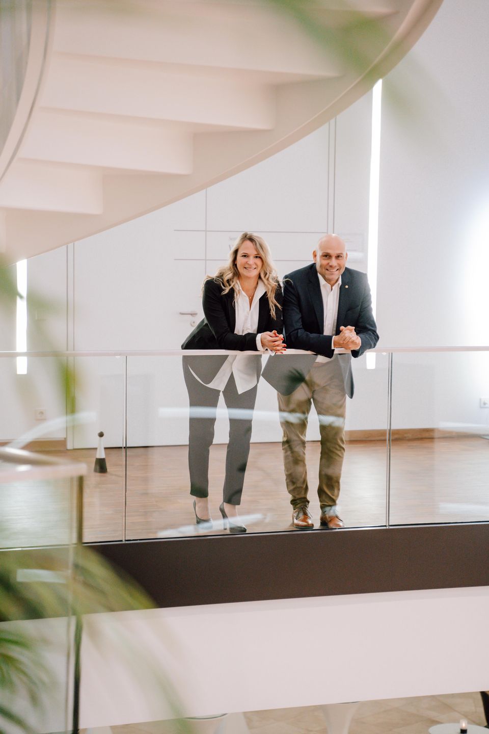 André Feller und eine Frau lehnen nebeneinander an der Glasbrüstung einer Galerie und lächeln in die Kamera.
